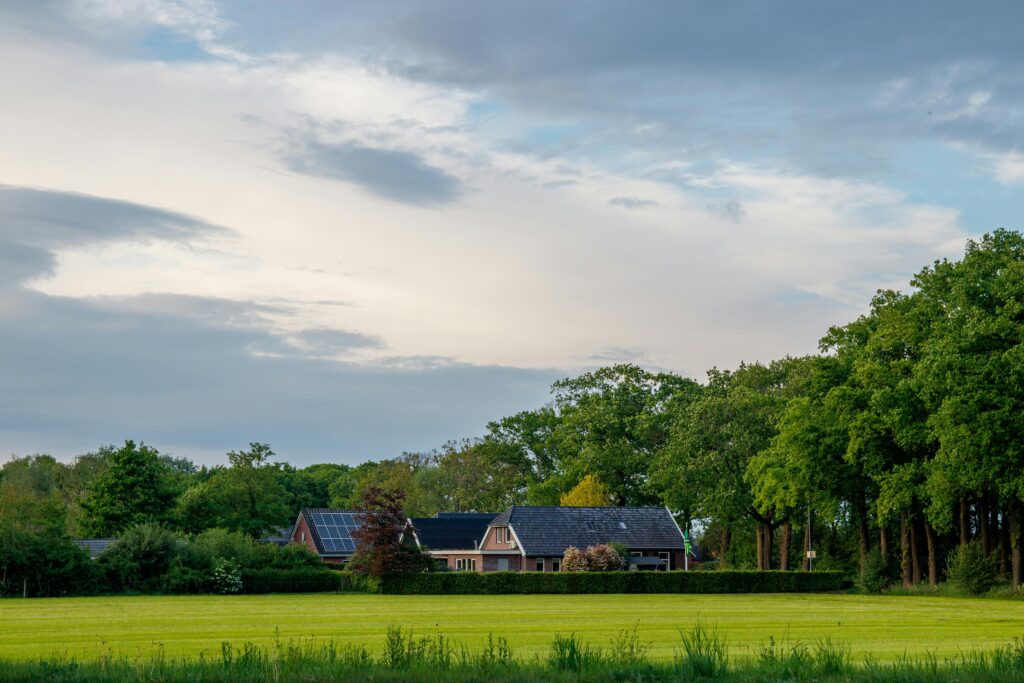 Charming rural home with solar panels in a lush green landscape under a cloudy sky.